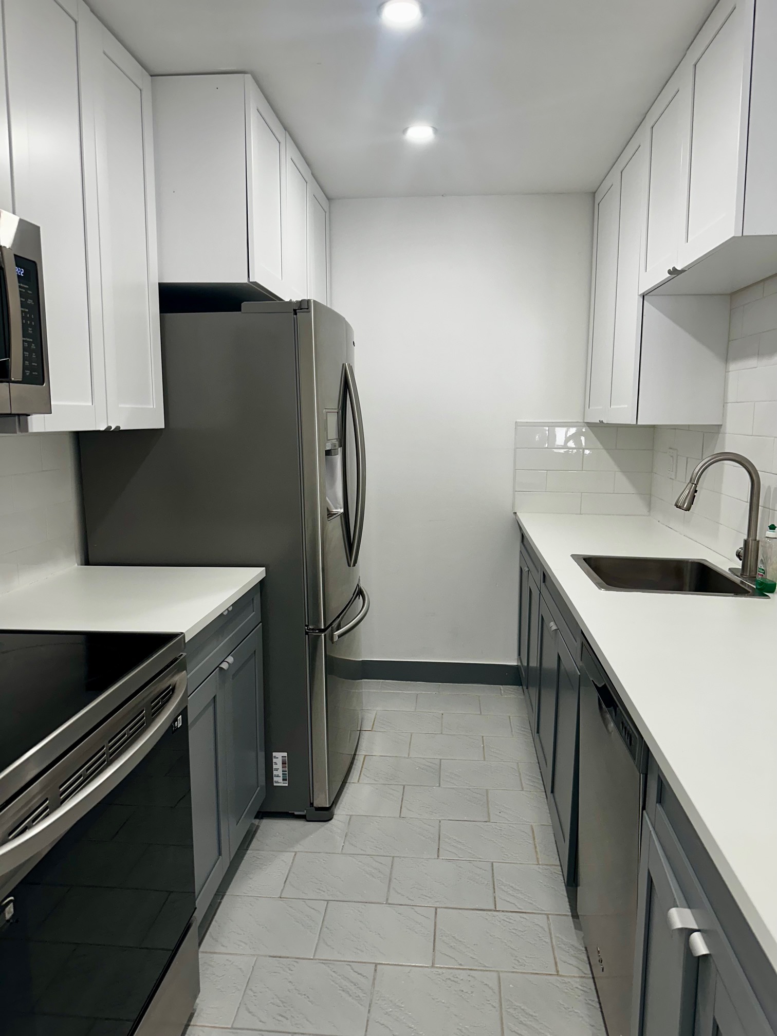 Renovated rental kitchen with white upper cabinets, gray lower cabinets, white countertops and stainless steel appliances.