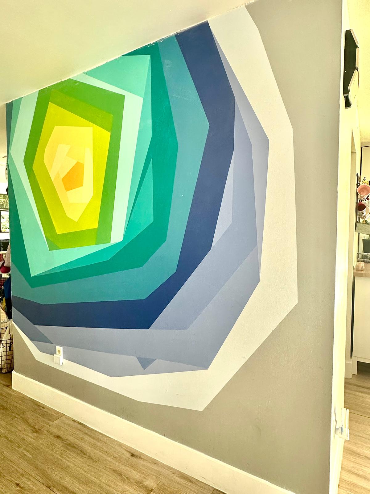 Geometric wall mural with layered blue, turquoise, green and yellow shapes creating a tunnel of light effect.